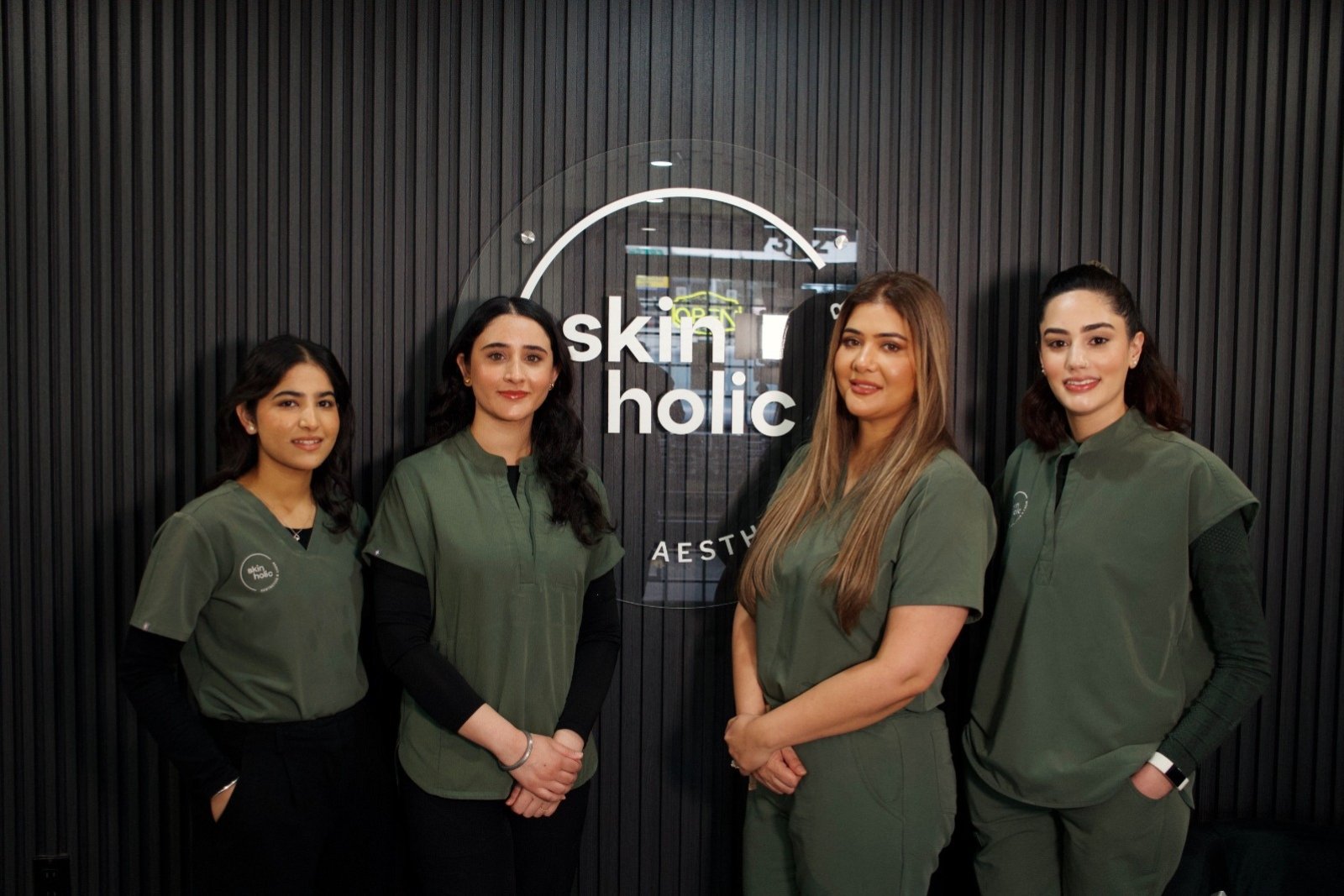 Four members of the Skinholic Aesthetics & Laser team standing together in front of the illuminated clinic sign.