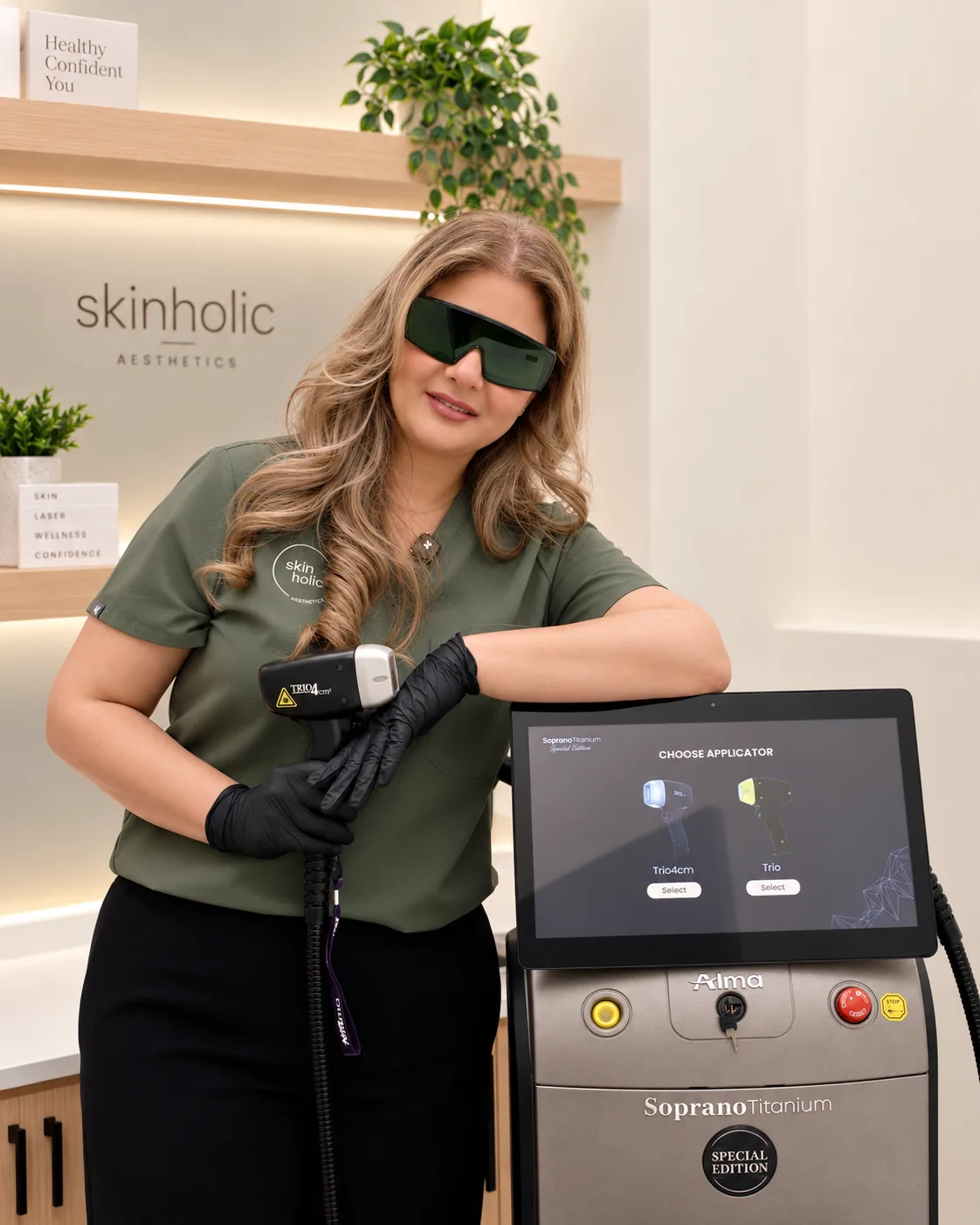 Practitioner in laser safety glasses holds a handpiece while leaning on a laser hair removal machine in a bright clinic