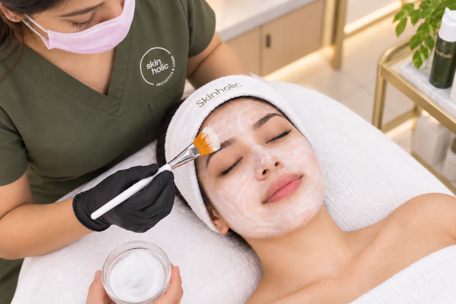Practitioner paints a white mask onto a woman's forehead with a fan brush during a brightening facial