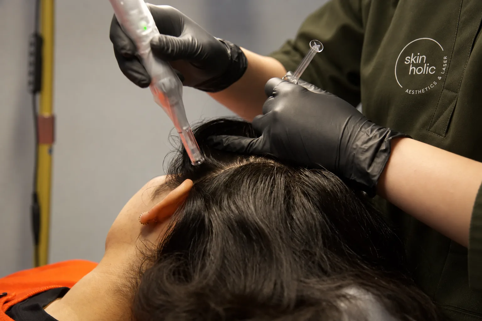 Gloved hands hold a microneedling pen to the scalp and a small clear applicator during DERIVE hair wellness