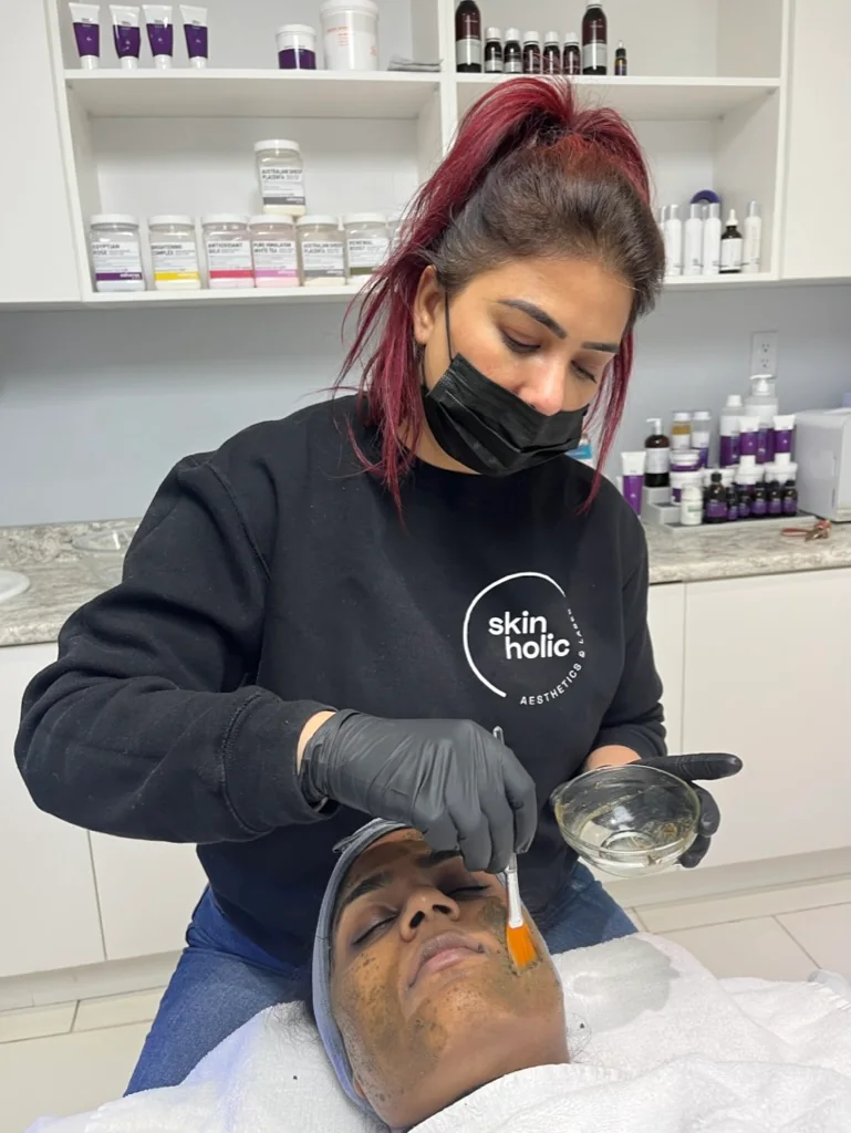 Skinholic aesthetician in gloves brushing a professional peel mask onto a reclined client's face in Surrey